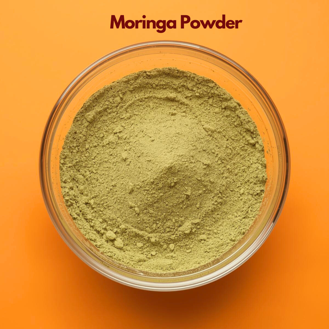 Overhead view of Moringa Powder in a clear glass bowl, displaying finely ground light green herbal powder with soft consistency on an orange backdrop. Nutrient rich botanical powder used in natural skincare masks, herbal cosmetics and Ayurvedic wellness blends.