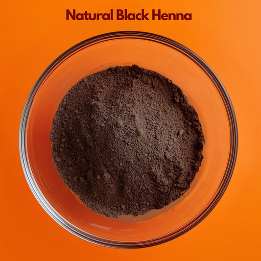  Top angle image of Natural Black Henna powder in a clear glass bowl, displaying deep brown finely milled herbal powder on a bright orange background. Plant based herbal hair color powder used in natural hair dye applications and Ayurvedic hair care formulations.
