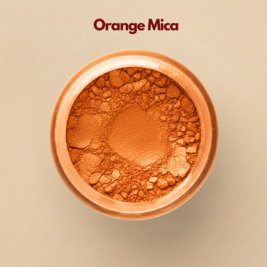 Close up top view of orange mica powder in a round container, displaying a vibrant metallic orange tone with fine reflective particles. The surface appears textured with small pressed and loose shimmer fragments. This orange mica powder for cosmetics is used to create luminous effects in eye shadow and highlighter.
