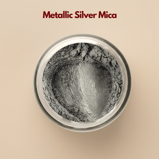 Top view of silver mica powder inside a round container, showing a soft metallic shimmer with a fine reflective texture. The surface appears slightly crinkled with natural mineral shine. This silver mica powder for cosmetics is used to add shimmer and luminosity to makeup and skincare formulations.