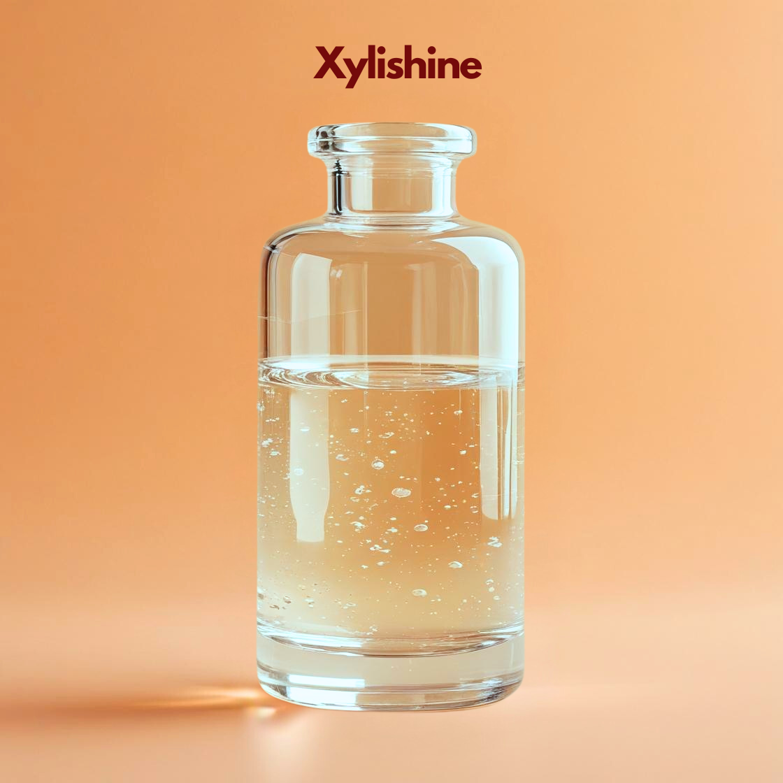 Transparent glass bottle filled with clear liquid labeled "Xylishine"  placed on a warm orange background with soft lighting reflections. Xylishine is a cosmetic haircare active ingredient used in formulations to strengthen hair improve shine and enhance hair health.