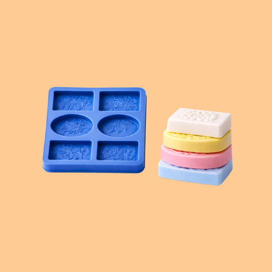 Blue silicone mini soap mould trays displayed with stack of small pastel colored oval soaps, flexible mold used for DIY soap crafting, handmade guest soaps, and artisan bath product manufacturing.