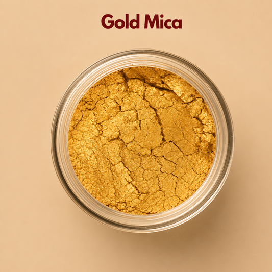 Close up top view of gold mica powder in a round container, displaying a rich metallic golden sheen with delicate reflective particles. The texture looks finely milled with visible natural mineral cracks across the surface. This gold mica pigment powder is used to create shimmer effects in cosmetics and beauty products.