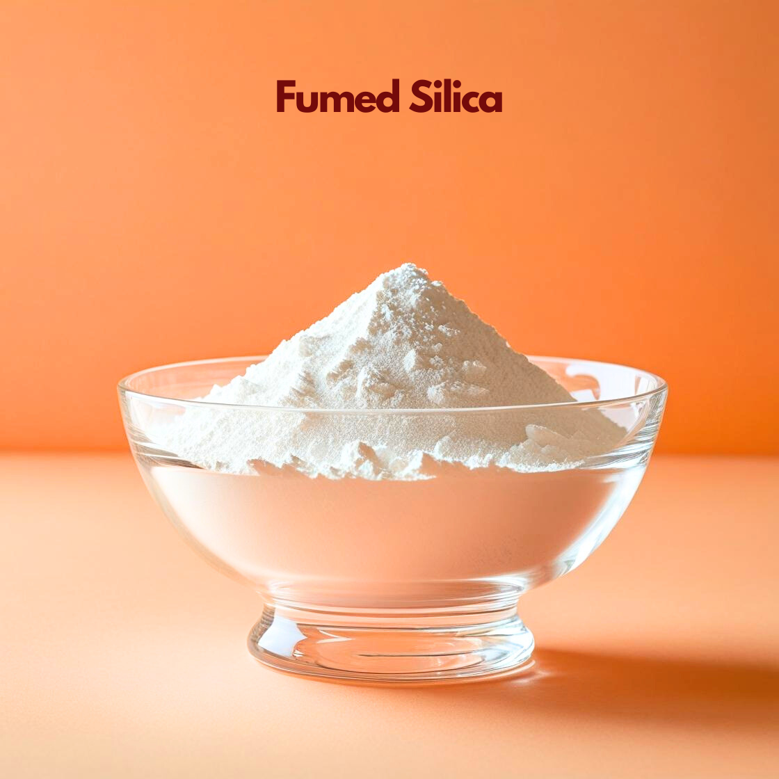 A clear bowl showcases a light, airy mound of "Fumed Silica" powder on an orange background. The powder has a delicate, almost weightless appearance with tiny textured clusters. In cosmetic products, fumed silica is used as a thickening and anti caking agent to improve stability and texture.