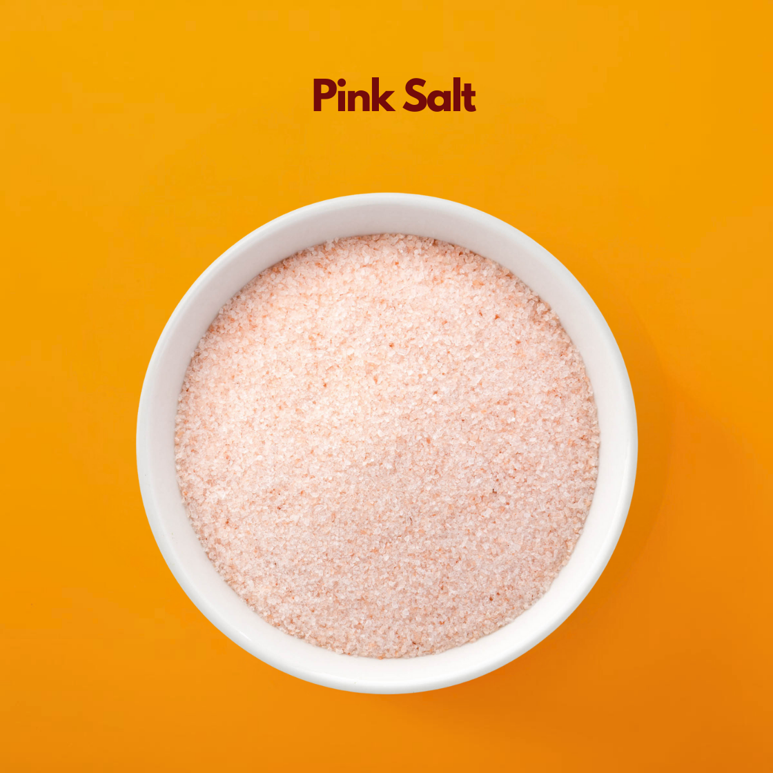  White bowl filled with fine pink Himalayan salt labeled "Pink Salt" placed on a bright orange background. Cosmetic pink salt is commonly used in bath salts body scrubs and spa formulations for exfoliation and mineral rich skincare treatments.