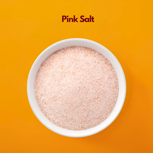  White bowl filled with fine pink Himalayan salt labeled "Pink Salt" placed on a bright orange background. Cosmetic pink salt is commonly used in bath salts body scrubs and spa formulations for exfoliation and mineral rich skincare treatments.