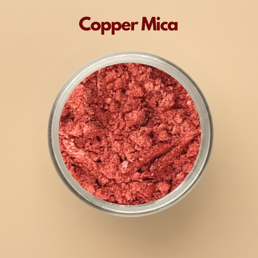 Copper mica powder with metallic shimmer texture displayed in a round transparent cosmetic jar on a beige background. Cosmetic grade copper mica pigment used in skincare formulations, soap making, makeup products, candles, lip gloss, and DIY cosmetic manufacturing. The image highlights rich copper shimmer with reflective metallic cosmetic pigment appearance.