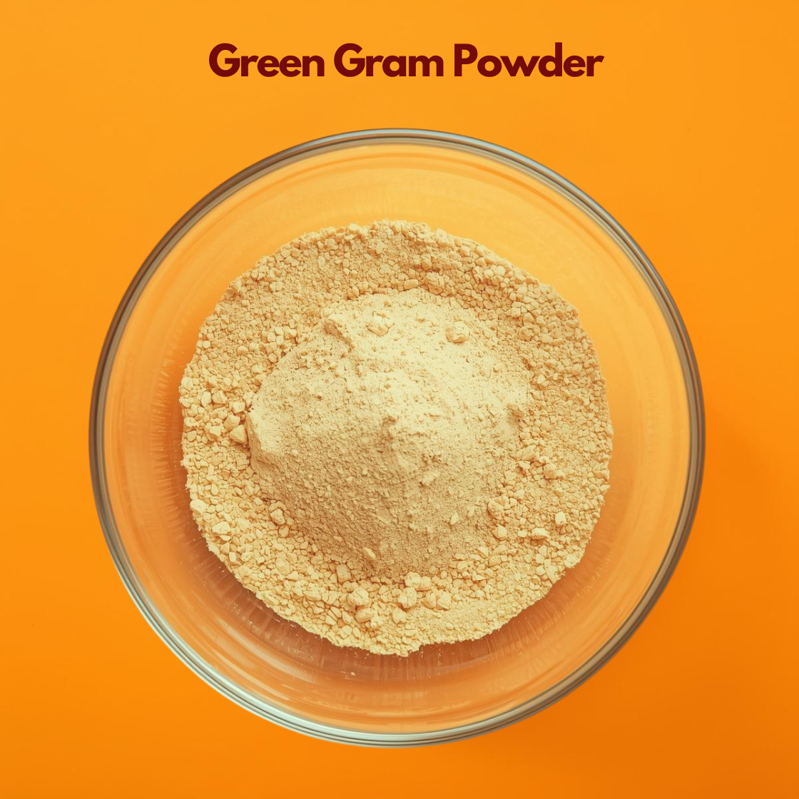 Overhead view of Green Gram Powder in a clear glass bowl on a vibrant orange background, displaying finely milled light yellow beige herbal powder with soft texture. Natural herbal powder used in face packs, gentle exfoliation treatments and cosmetic skincare blends.
