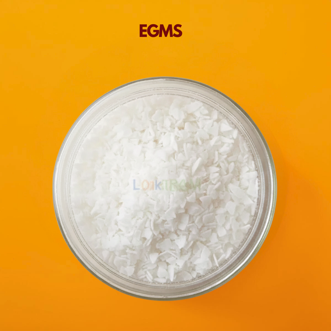  A top down view of a clear bowl filled with white, slightly glossy flakes layered densely over one another on an orange background. The flakes are thin and uneven, giving a soft, textured appearance. EGMS (Ethylene Glycol Monostearate) is commonly used in cosmetic and shampoo formulations for pearlizing and texture enhancement.
