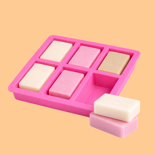 Pink silicone soap mold with six rectangular cavities partially filled with pastel colored handmade soap bars alongside stacked soap bars, mold used for DIY soap crafting, melt and pour soap making and cosmetic soap production.