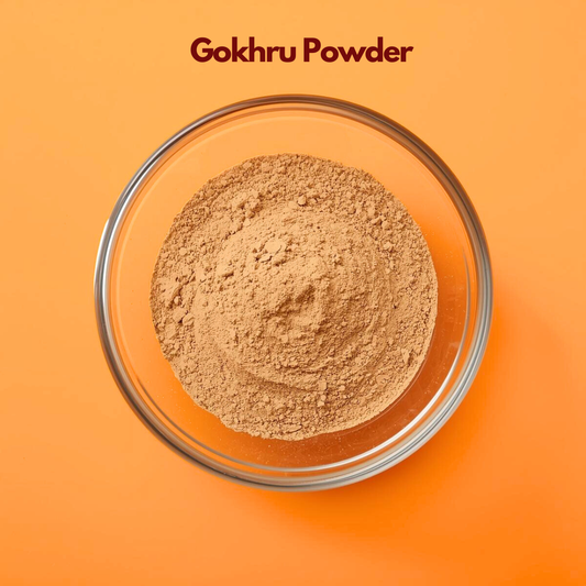 Overhead close up of Gokhru Powder in a glass bowl, displaying its fine light brown herbal texture on a clean orange surface. Traditional Ayurvedic botanical powder used in natural formulations and herbal powder blends.