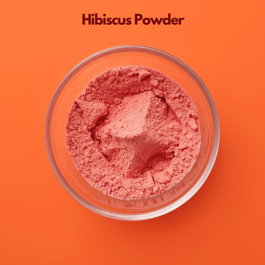  Top view of Hibiscus Powder in a transparent glass bowl placed on an orange background, displaying vibrant pink finely ground floral powder with soft texture. Natural hibiscus flower powder used in herbal hair masks, scalp conditioning treatments, and plant based cosmetic formulations.