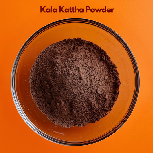 Overhead image of Kala Kattha Powder placed in a clear glass bowl, displaying rich dark brown finely ground herbal powder on a bright orange surface. Traditional botanical powder used in natural cosmetic blends, herbal preparations and Ayurvedic skincare formulations.