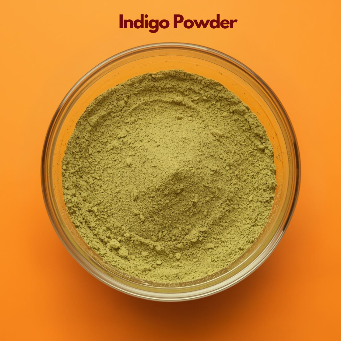Top angle image of Indigo Powder placed in a transparent bowl, showing finely milled greenish herbal powder against a vibrant orange background. Natural botanical indigo powder used for herbal hair coloring, grey coverage, and plant based cosmetic hair formulations.
