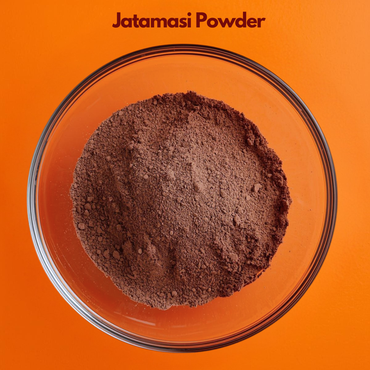 Overhead close up of Jatamasi Powder in a transparent bowl, featuring dark brown finely ground herbal powder against a vibrant orange surface. Ayurvedic botanical ingredient commonly used in natural hair care and traditional herbal preparations.