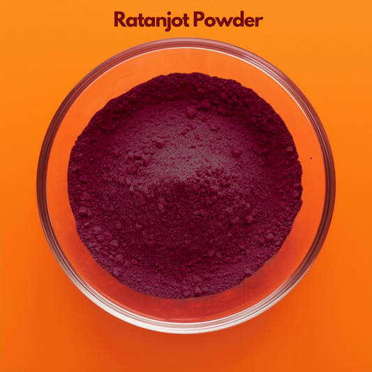 Overhead image of Ratanjot Powder in a clear glass bowl, displaying dark burgundy finely milled herbal powder on an orange background. Botanical coloring herb powder used in natural cosmetic formulations, herbal oils and Ayurvedic skincare preparations.