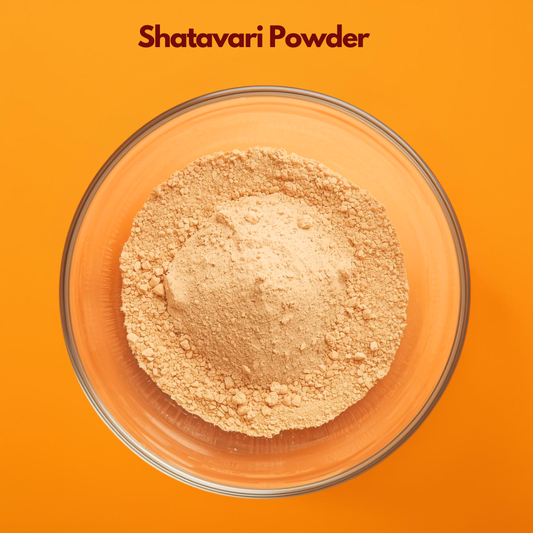 Top view of Shatavari Powder in a transparent bowl on a vibrant orange surface, revealing finely ground beige herbal powder with slightly grainy texture. Ayurvedic botanical powder used in traditional wellness blends and natural cosmetic formulations.