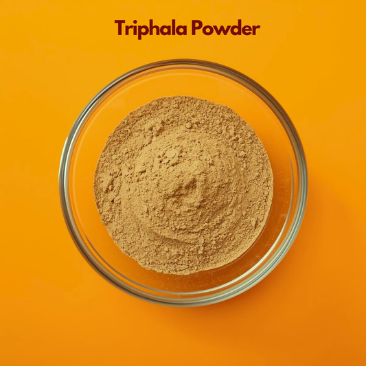 Overhead view of Triphala Powder in a clear glass bowl, showing finely ground beige brown herbal blend on a vibrant orange surface. Traditional Ayurvedic herbal powder combination used in natural wellness preparations and botanical cosmetic formulations.