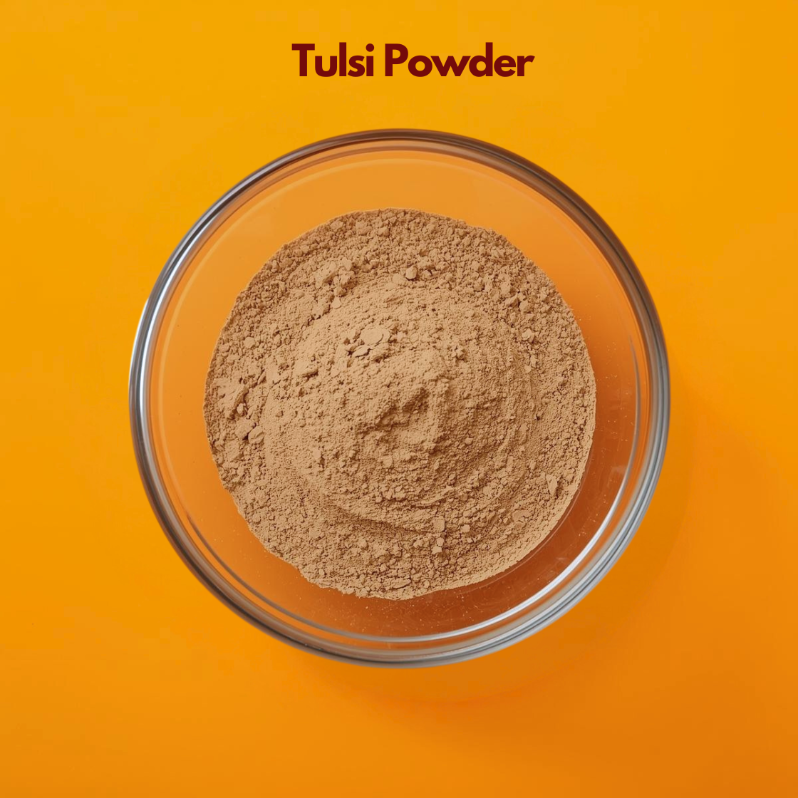 Overhead close up of Tulsi Powder in a clear glass bowl, displaying finely milled green herbal powder on an orange surface. Botanical herbal powder widely used in acne care face packs, herbal skincare treatments and Ayurvedic cosmetic formulations.